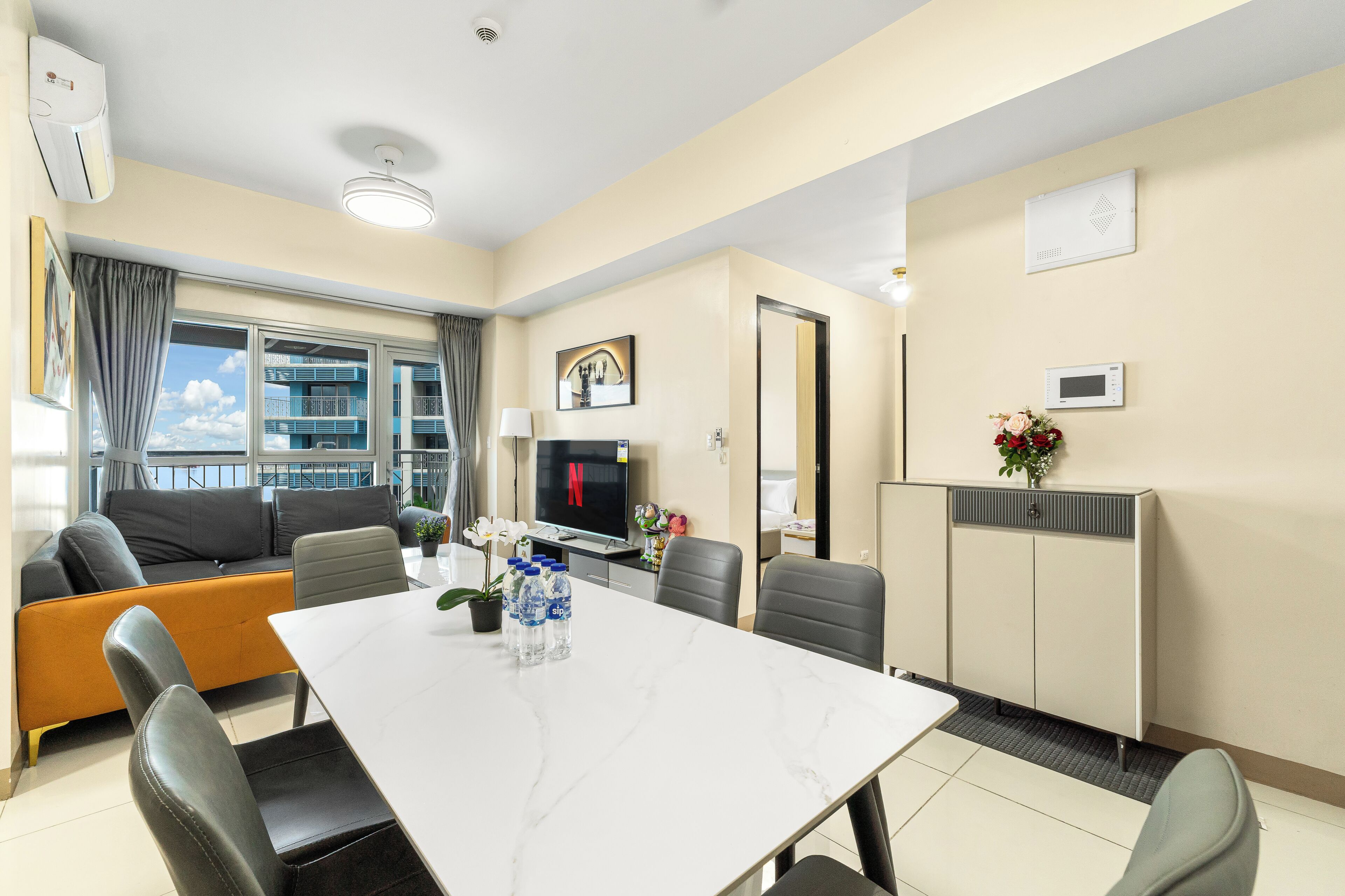 A hotel room with a dining area, a sofa, a TV, and a view of the outside.