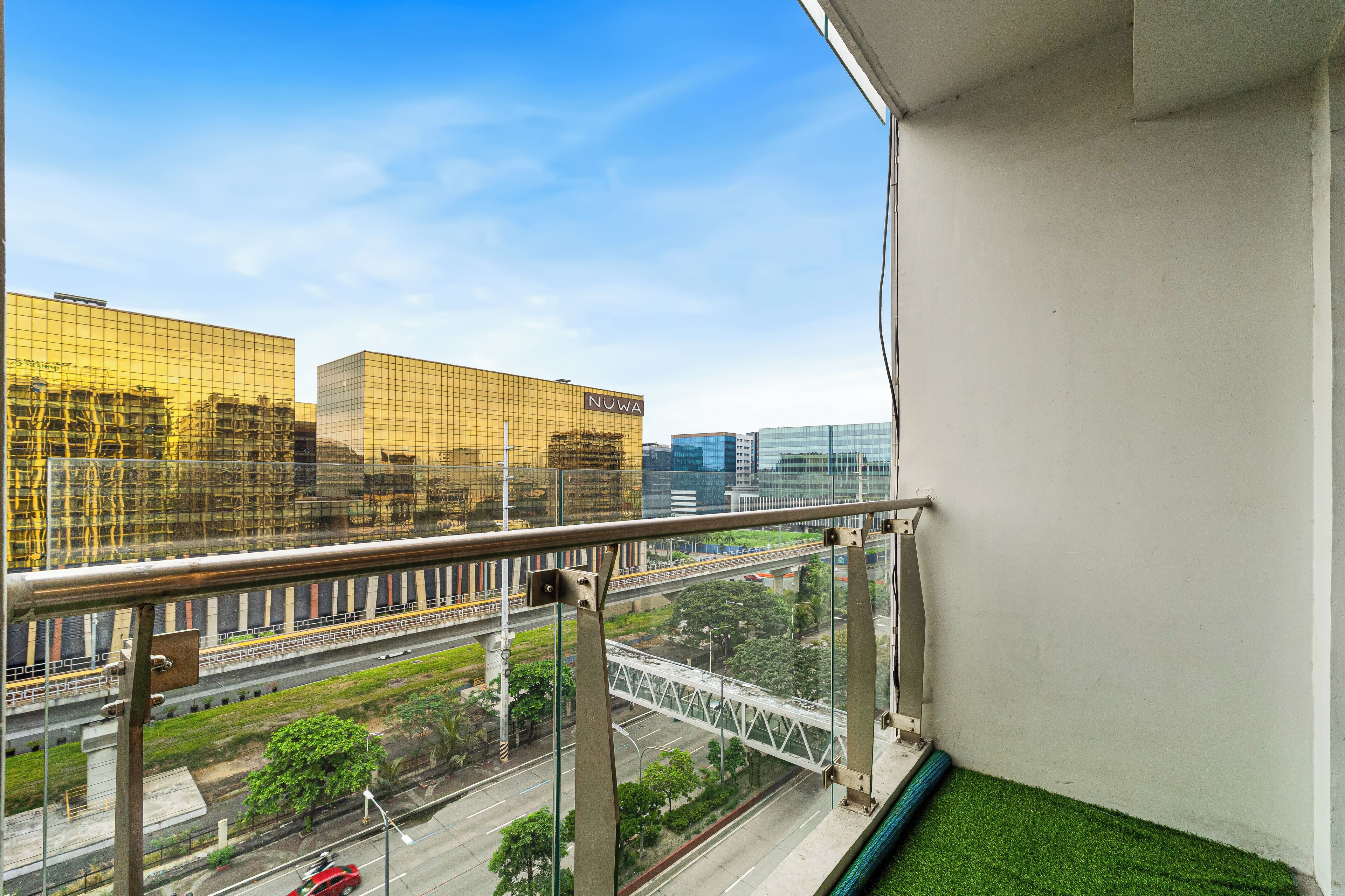 Un balcon offrant une vue sur le paysage urbain, avec notamment un bâtiment portant l’inscription « NUWA ».