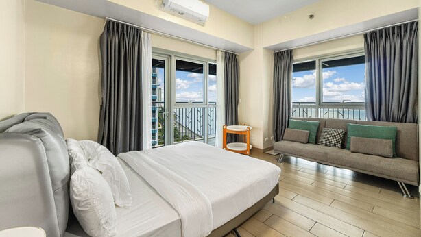 A hotel room with a bed, a sofa, a small table, and a balcony with a view. - Spacious & High-Floor Hotel near City of Dreams, Airport, Okada, and Solaire Casino (Parañaque)