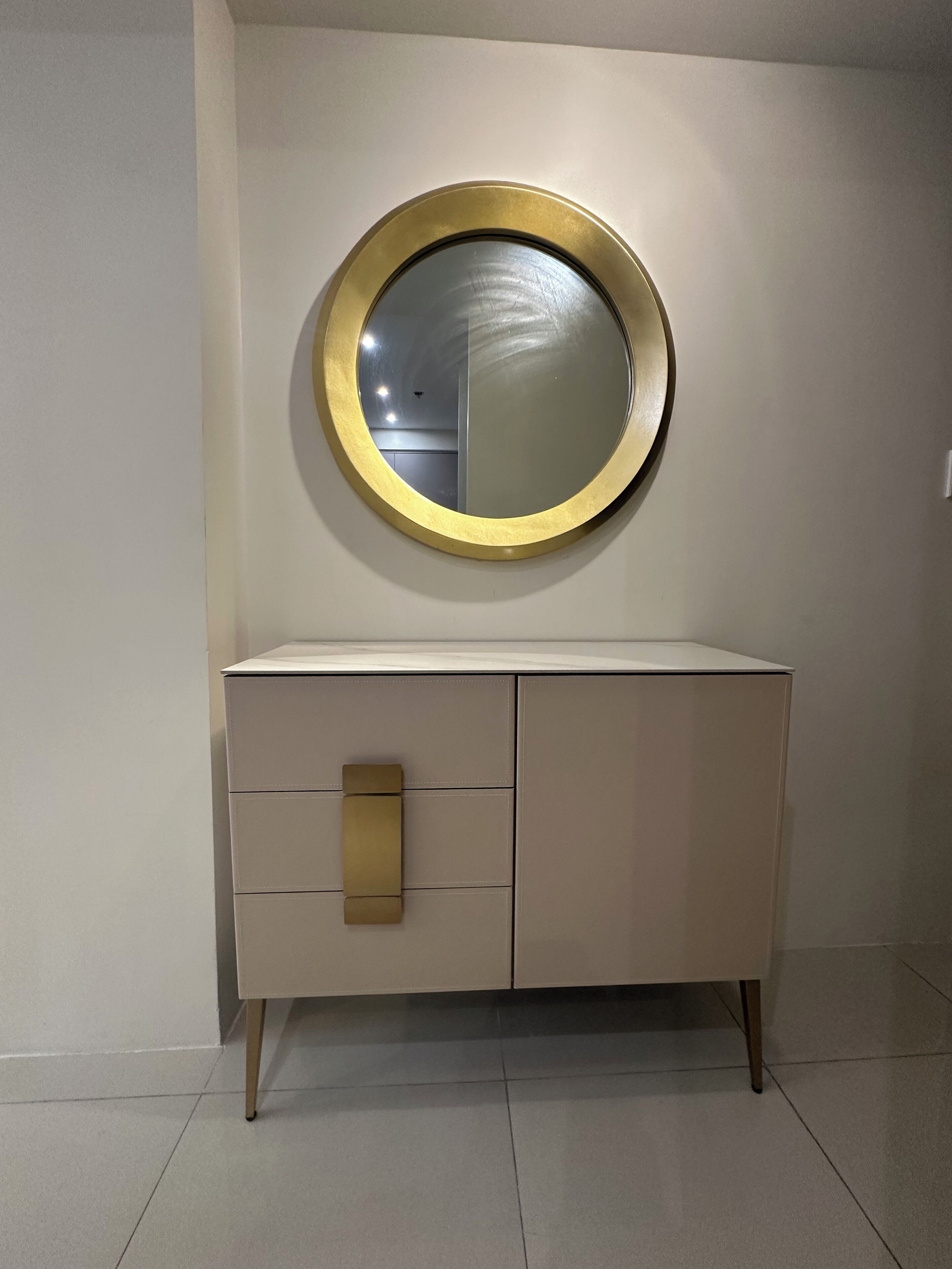 A white cabinet with a gold-framed mirror above it.