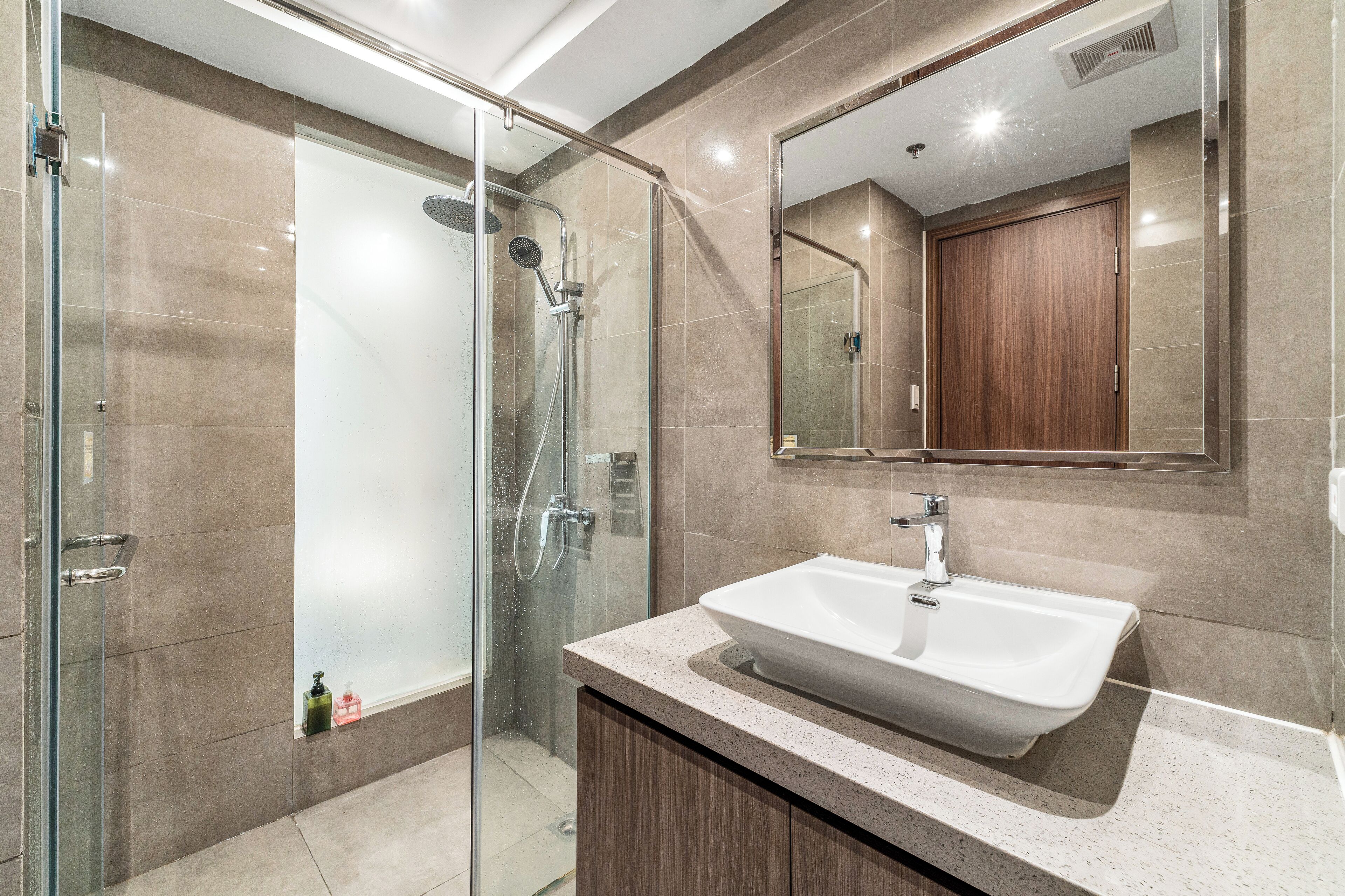 A modern bathroom with a glass shower enclosure, a white sink, and a wooden vanity.