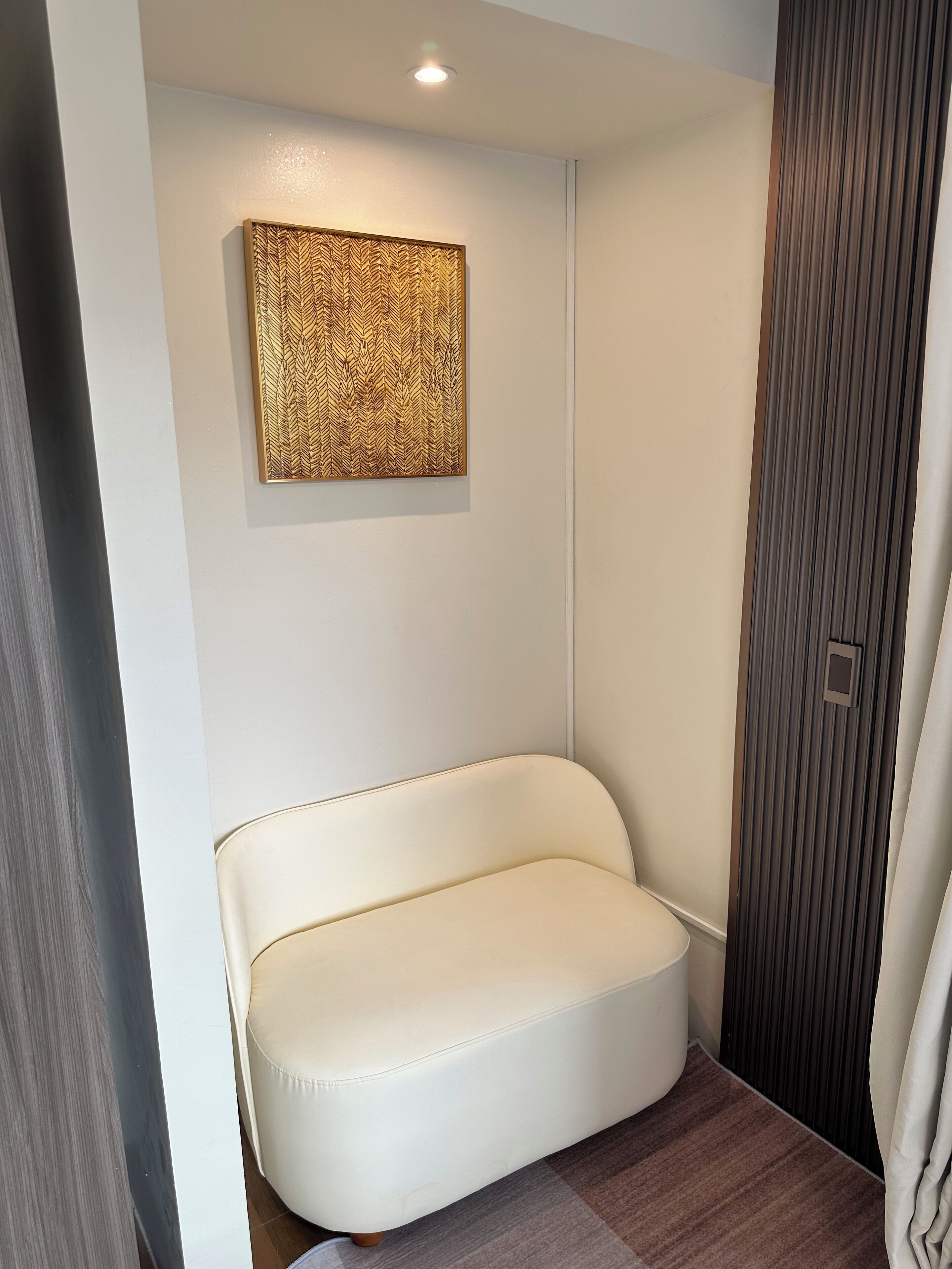 Una habitació moderna amb un sofà de pell blanca, una obra d'art amb textura a la paret i un panell vertical amb un petit obertura quadrada.