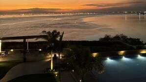 A sunset view from a hotel balcony overlooking a beach with a swimming pool and lounge area. - Spacious & High-Floor Hotel near City of Dreams, Airport, Okada, and Solaire Casino (Parañaque)