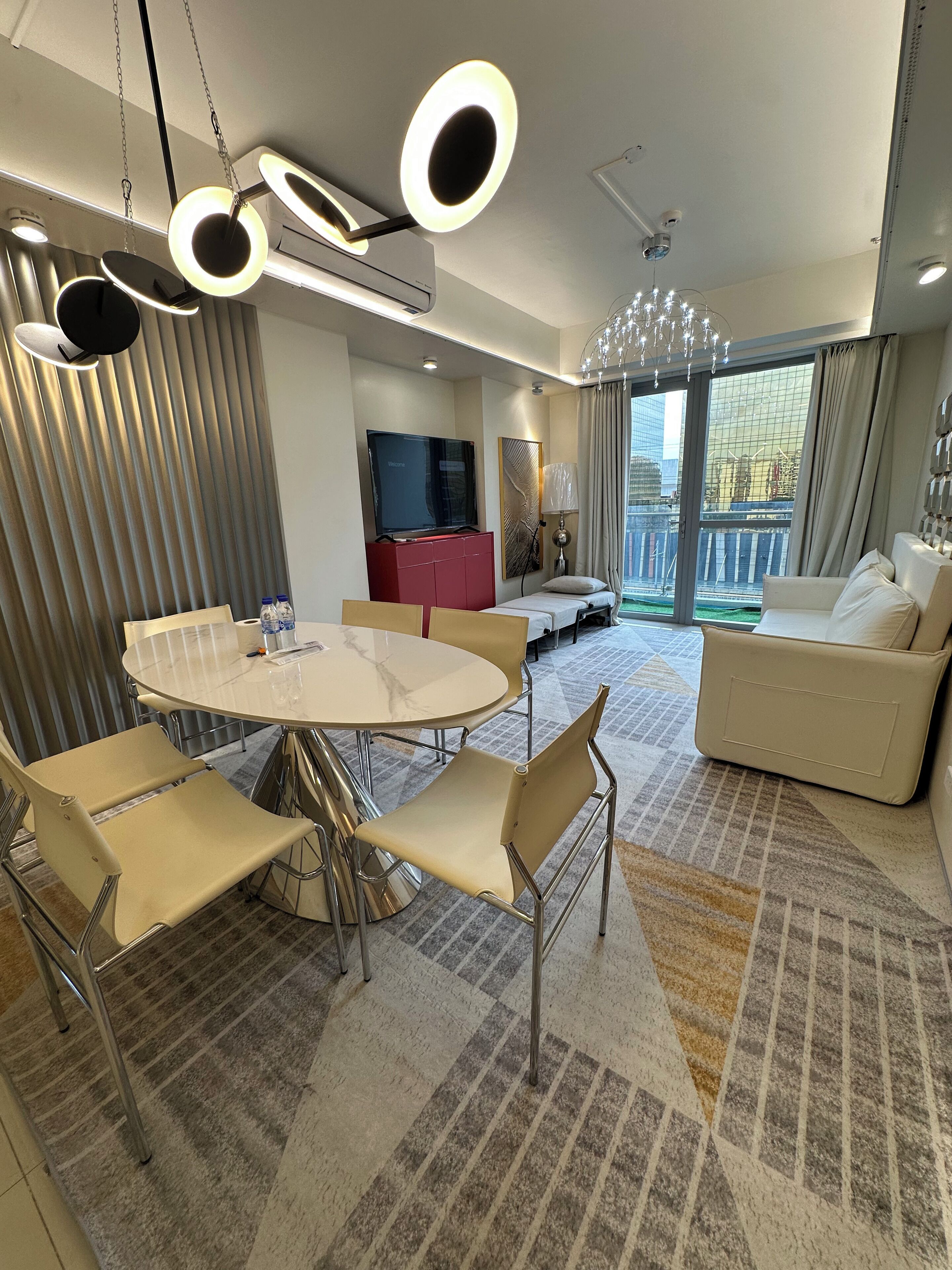 A modern hotel room with a dining area, a sofa, and a TV.