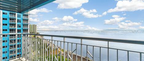 A balcony with a metal railing overlooking a body of water and a distant shoreline.