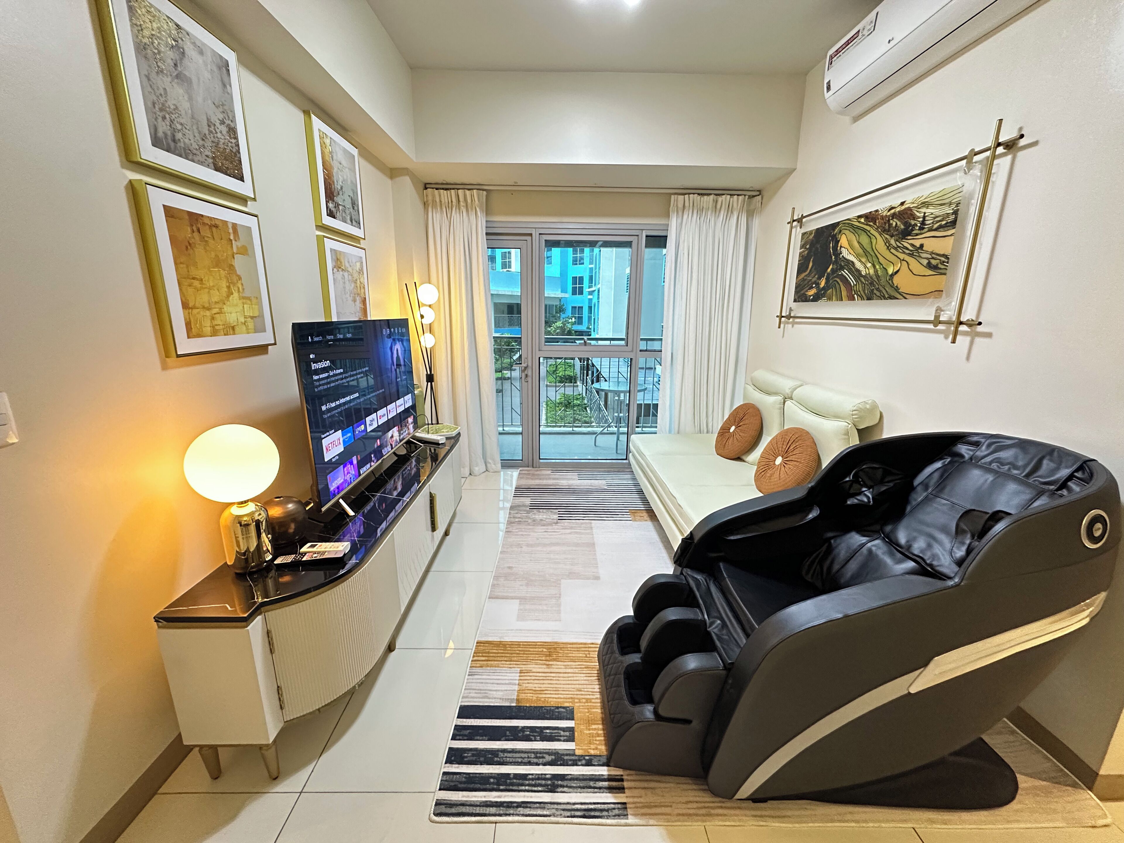 A modern living room with a massage chair, a TV on a stand, and a balcony with a view.