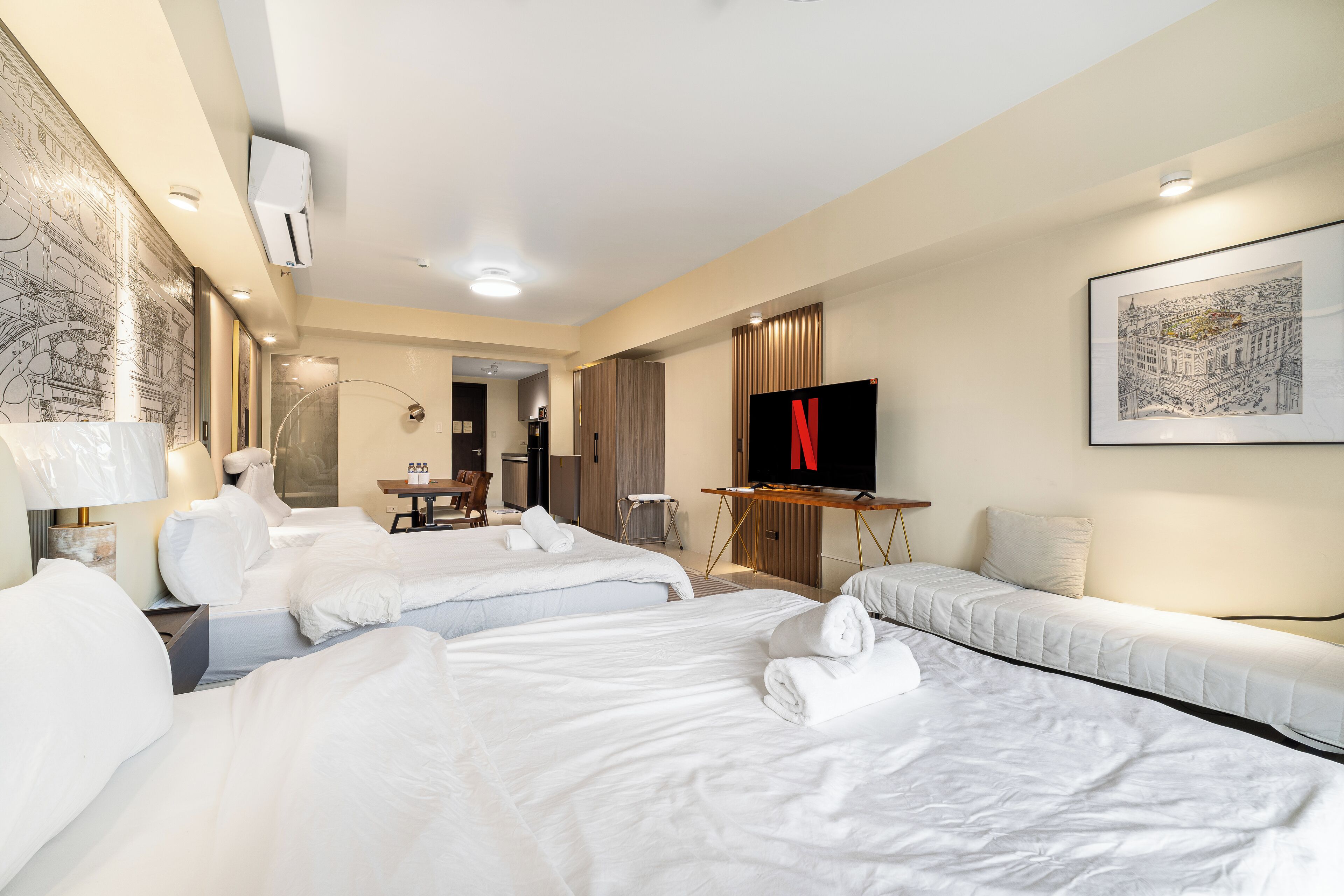 Ein Hotelzimmer mit drei Betten, einem Fernseher und einer Essecke.