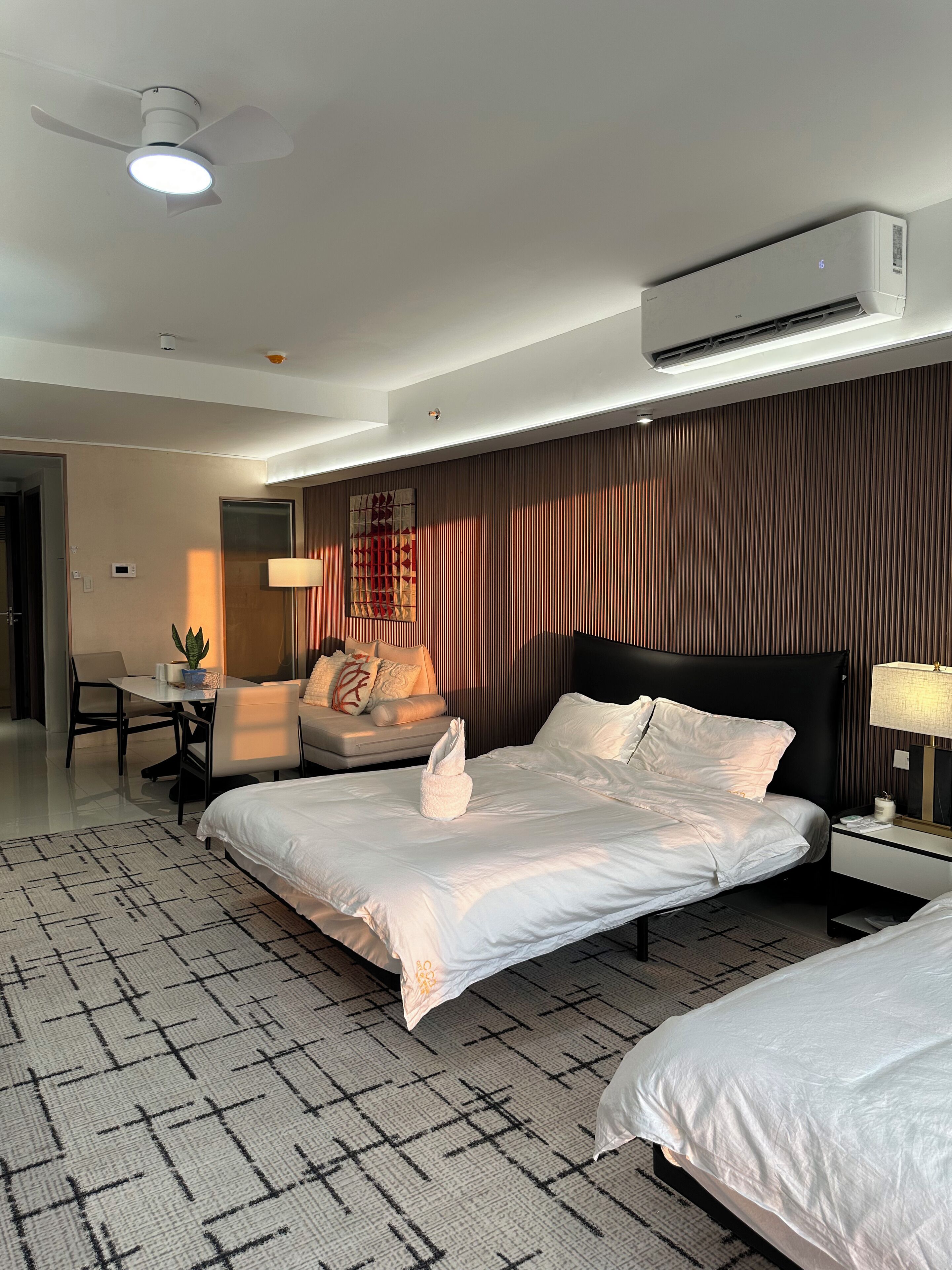 Een hotelkamer met een bed, een bureau, een stoel, een lamp en een airconditioner.