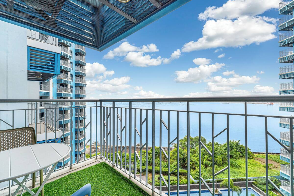 Ein Balkon mit Blick auf ein Schwimmbad und Grünflächen, einem Tisch und Stühlen.