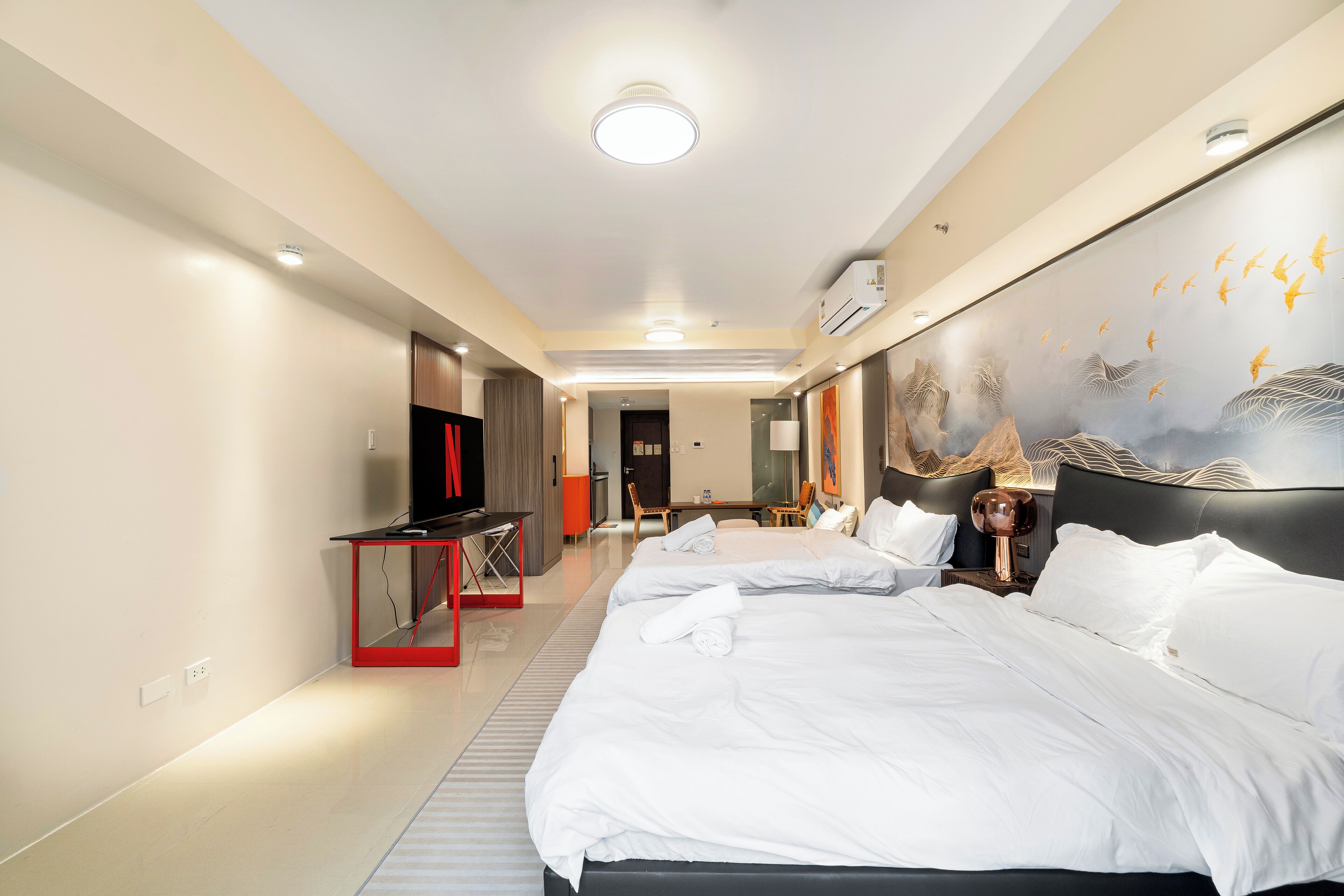 A hotel room with two beds, a desk, a TV, and a mural on the wall.
