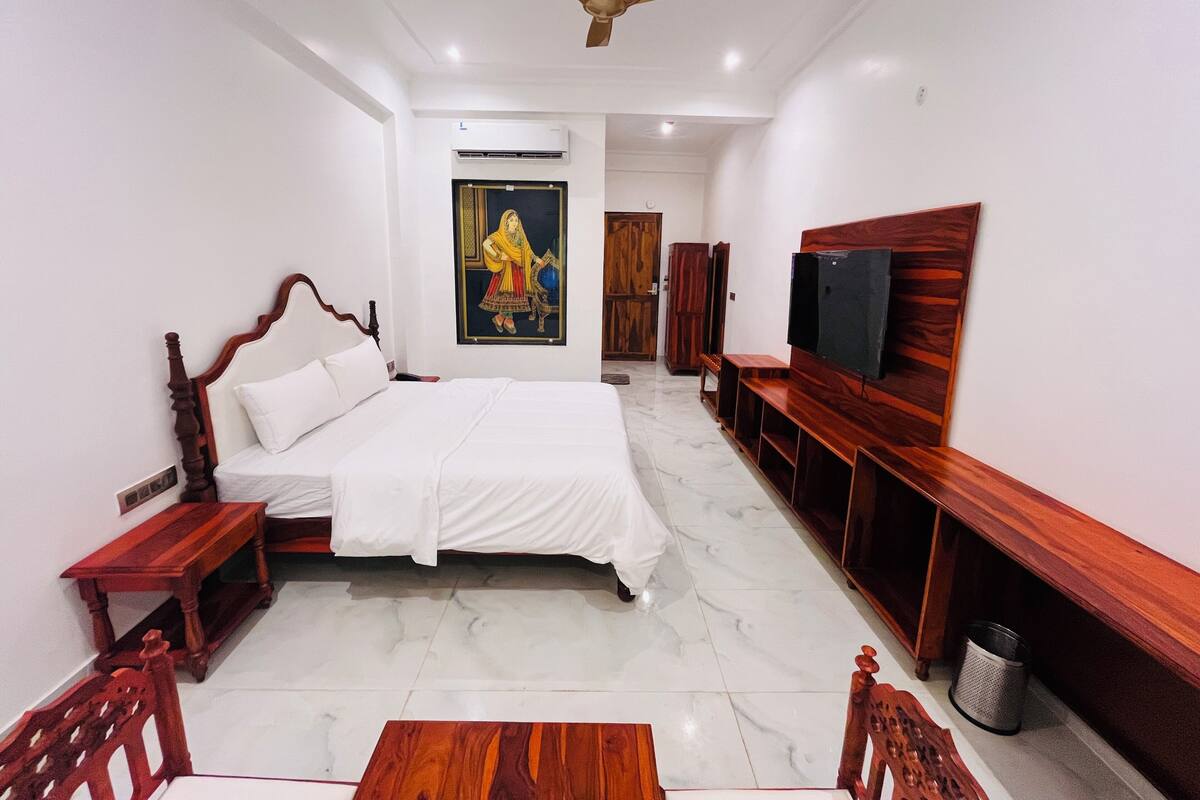 A bedroom with a bed, a wooden bench, a television, and a ceiling fan.