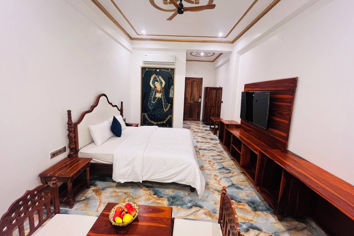 A hotel room with a bed, a TV, a wooden bench, a table with fruit, and a patterned floor.