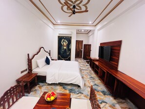 A hotel room with a bed, a TV, a wooden bench, a table with fruit, and a patterned floor.
