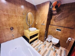 A bathroom with a bathtub, a sink with a mirror, a toilet, and a shower area.