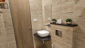 A bathroom with a wooden door, a white sink, a mirror, and a small shelf with plants. - Hotel Siyaram (Ayodhya)