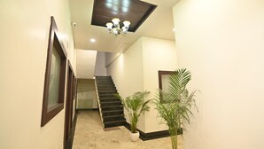 A hallway with a staircase, a chandelier, and potted plants. - Hotel Siyaram (Ayodhya)