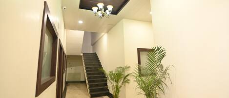 A hallway with a staircase, a chandelier, and potted plants.