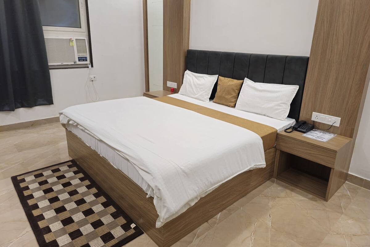 Moderni hotellihuone, jossa on suuri sänky, yöpöytä, jossa on puhelin, ja pieni työpöytä, jossa on lamppu.