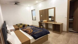 A modern bedroom with a large bed, a vanity, a ceiling fan, and a door leading to another room. - Hotel Siyaram (Ayodhya)