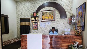 A reception desk with a man seated behind it, a framed picture above the desk, and a decorative statue to the right. - Hotel Siyaram (Ayodhya)