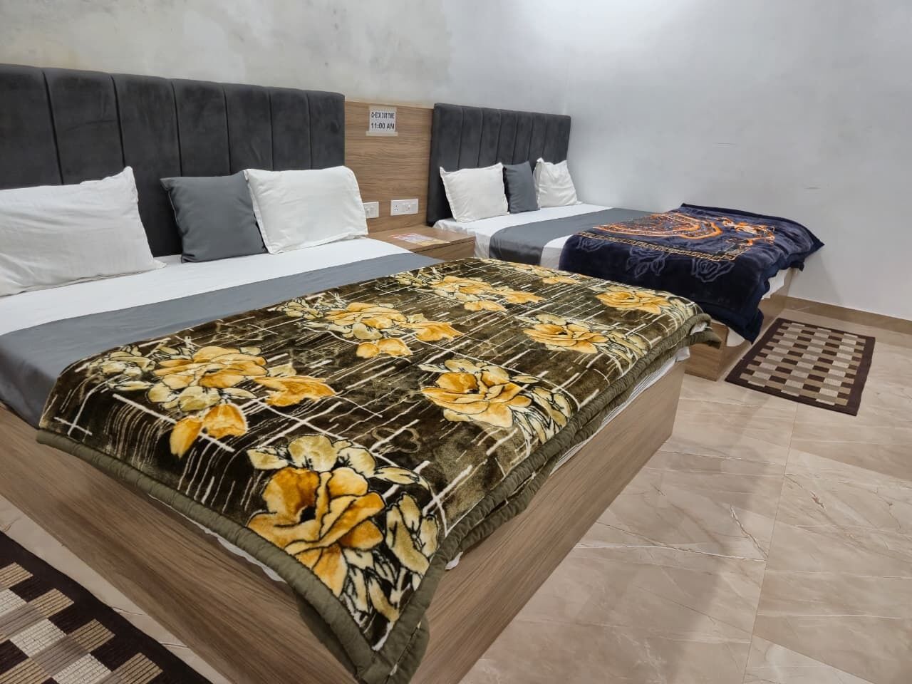 A hotel room with two beds, each with a headboard, a large floral-patterned bedspread, and a checkered rug on the floor.