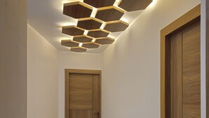 A hallway with a wooden door, a wall-mounted hexagonal light fixture, and a tiled floor. - Hotel Siyaram (Ayodhya)