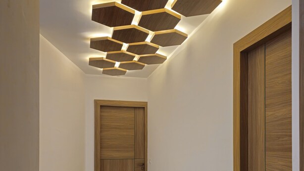 A hallway with a wooden door, a wall-mounted hexagonal light fixture, and a tiled floor. - Hotel Siyaram (Ayodhya)