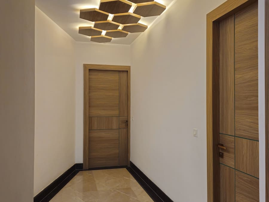 Un couloir avec une porte en bois, un luminaire hexagonal fixé au mur et un sol carrelé.