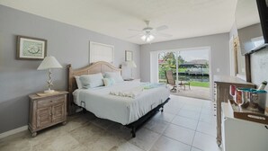 Ein Schlafzimmer mit Bett, Nachttischen, einem Deckenventilator und Blick auf einen Pool und Grünflächen.