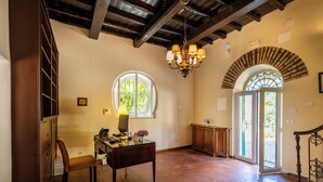 A spacious room with a wooden desk, a chair, a chandelier, and a large window. - Tenuta dell'inviolata (Velletri)