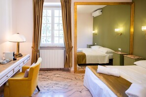 Et hotelværelse med en seng, et skrivebord med lampe, en stol, et vindue med gardiner og et spejl.