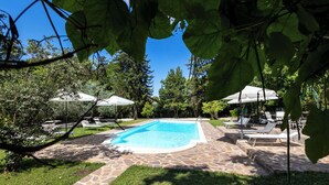 A swimming pool with stone tiles, surrounded by grass and trees, and shaded by umbrellas. - Tenuta dell'inviolata (Velletri)