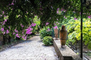 A cobblestone pathway in a garden with flowering plants and two large vases on stands. - Tenuta dell'inviolata (Velletri)