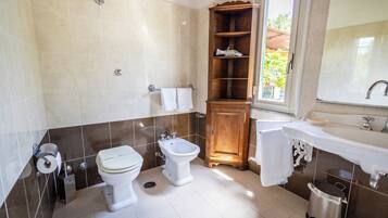 Et badeværelse med to toiletter, et pissoir, et træskab, en vask og et vindue.