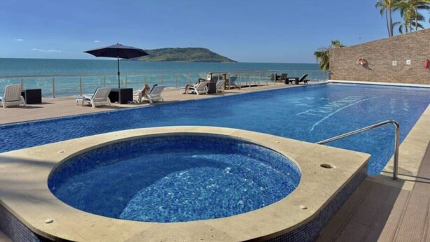 A swimming pool with lounge chairs and a hot tub, overlooking the sea.