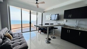 A modern kitchen with a dining area, large windows, and a view of the ocean.