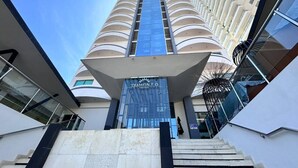 A modern hotel entrance with a glass facade, a prominent sign, and a staircase leading up to the entrance.