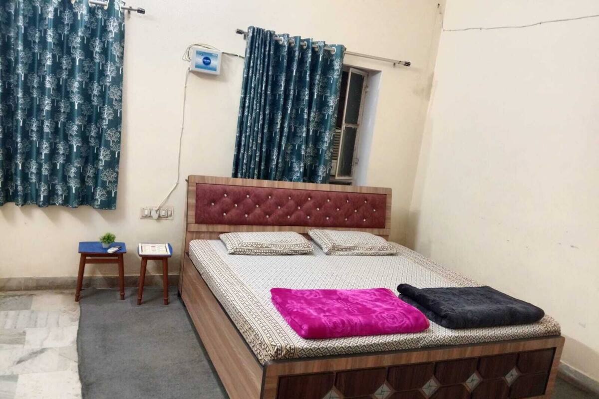 Ein Schlafzimmer mit Bett, Fenster, einem kleinen Tisch und einer Wandklimaanlage.