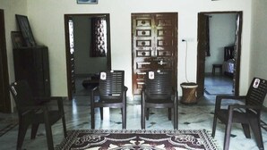 A room with two black plastic chairs, a patterned rug, a wooden door, and a cabinet. - Shyam Luxurious Huts & Guest House (Shri Madhopur)