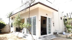 A single-story building with a flat roof, large windows, and a small porch area. - Shyam Luxurious Huts & Guest House (Shri Madhopur)