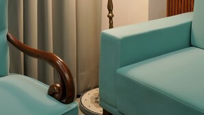 A room with a teal upholstered chair, a wooden slatted bench, and a decorative brass lamp with a patterned shade. - Hotel Devaan (Sirsa)