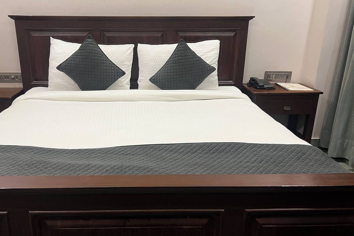 A hotel room with a large bed, two bedside tables, a telephone, and a nightstand with a lamp.