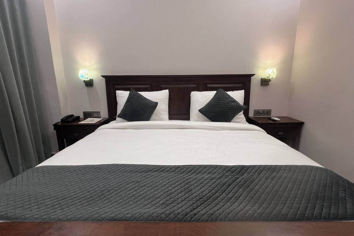 A hotel room with a large bed, two bedside tables, a nightstand, a lamp, and a curtain.