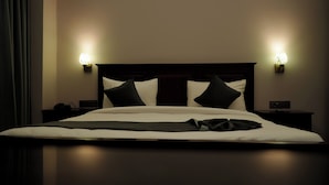A neatly made bed with white and black bedding, two bedside tables with lamps, and a dark wooden headboard. - Hotel Devaan (Sirsa)