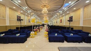 A banquet hall with rows of blue tables and chairs, a chandelier, and floral decorations. - Hotel Devaan (Sirsa)