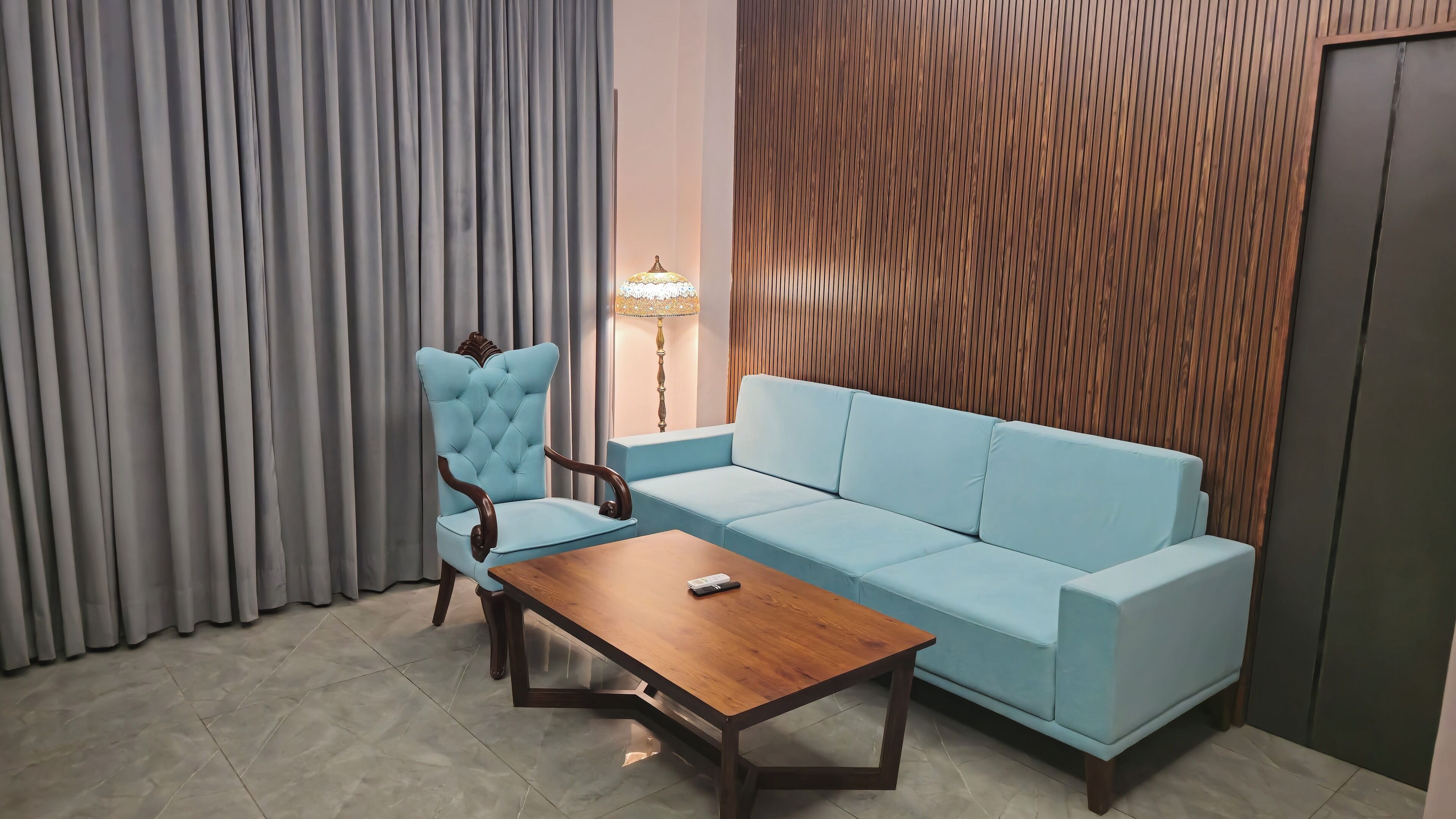 Ein Zimmer mit einem hellblauen Sofa, einem Holztisch und einem gesteppten Sessel.