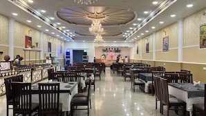 A spacious restaurant with multiple dining tables and chairs, a decorative ceiling, and wall-mounted artwork. - Hotel Devaan (Sirsa)