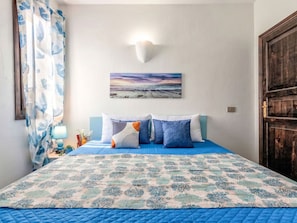 Un dormitorio con cama, mesita de noche, lámpara y un cuadro en la pared.