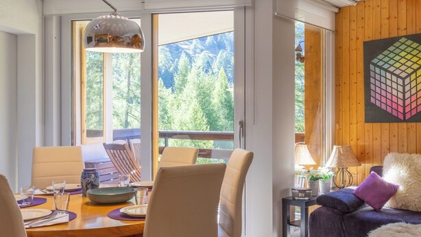 Una sala de estar moderna con comedor, ventanas amplias con vista a árboles y una pared de acento de madera.