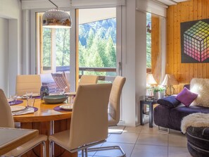 A modern living room with a dining area, large windows with a view of trees, and a wooden accent wall.